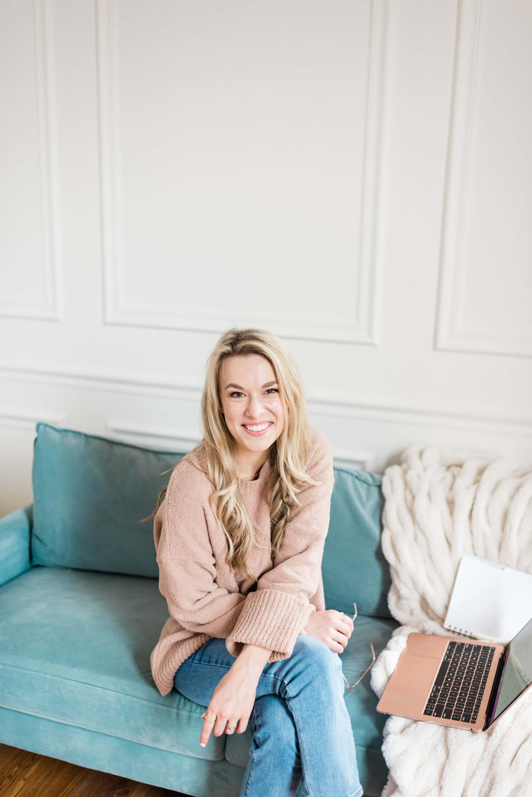 Woman on a blue couch wearing a pink sweater. She is smiling at the camera